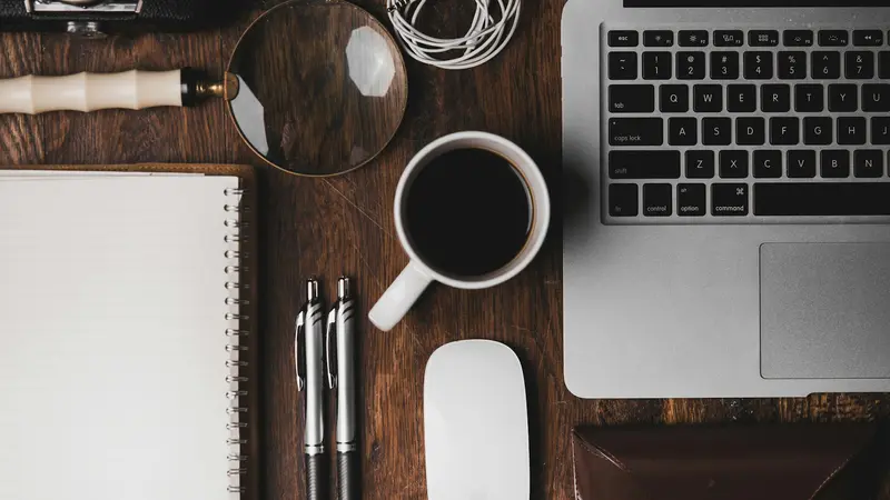 Tidy wooden desk with a laptop, notebook and a cup of coffee