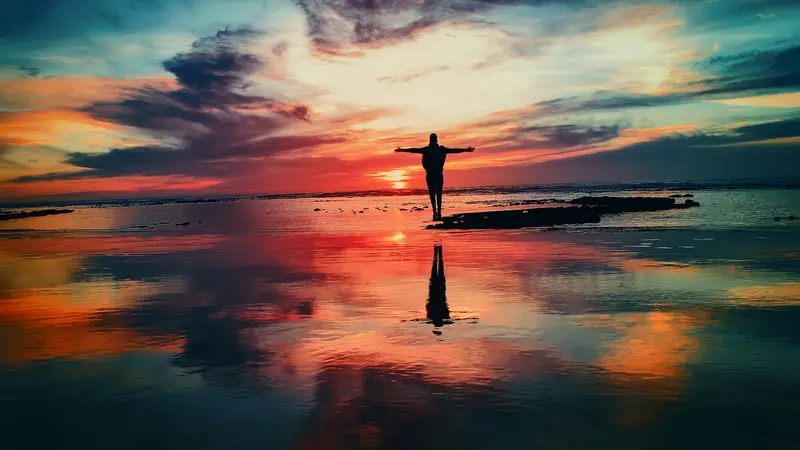 Person standing on calm water reflecting a colorful sunset sky